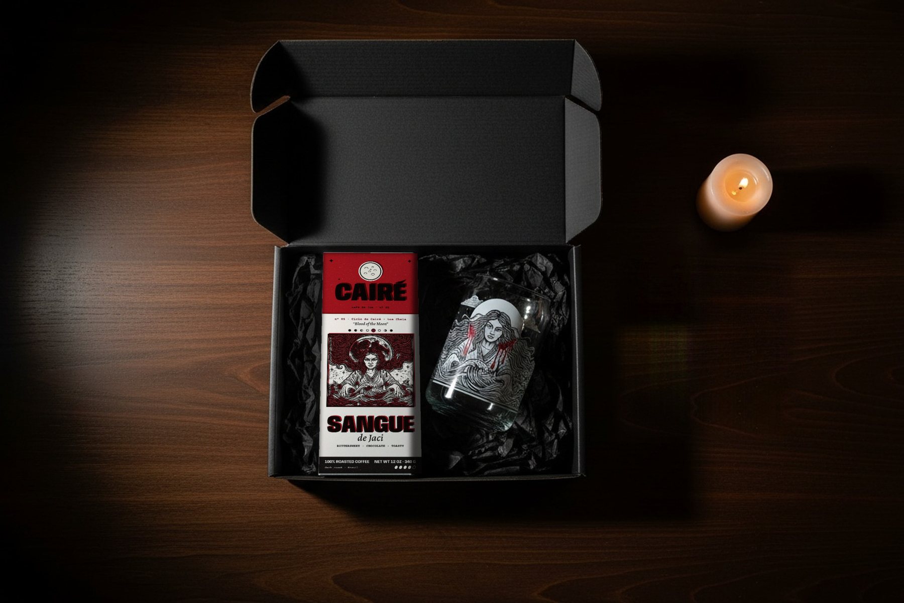 From above, by candlelight: an open black box lined with black tissue, the Sangue de Jaci coffee on one side and Jaci’s can glass on the other